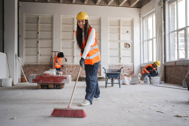 Female cleaner sweeping construction debris from unfinished room